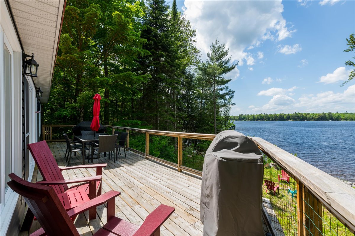 A wood deck with red Muskoka chairs face the lake