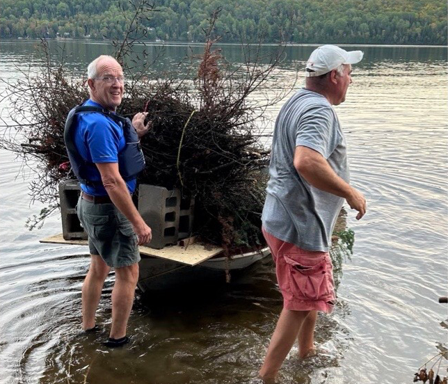 Two men in the lake with a boat full of sticks