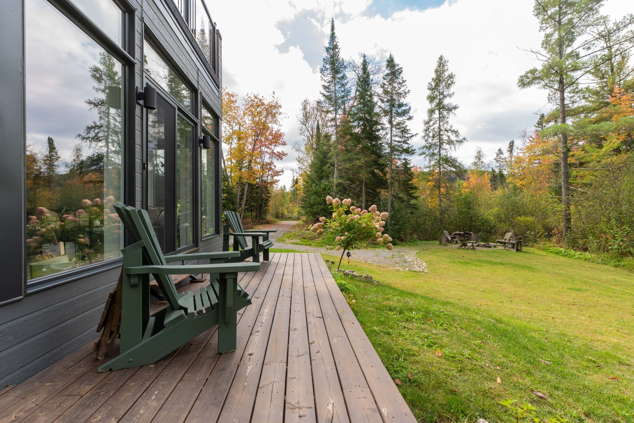 Green Muskoka chairs on a slim deck look out onto a grassy lawn