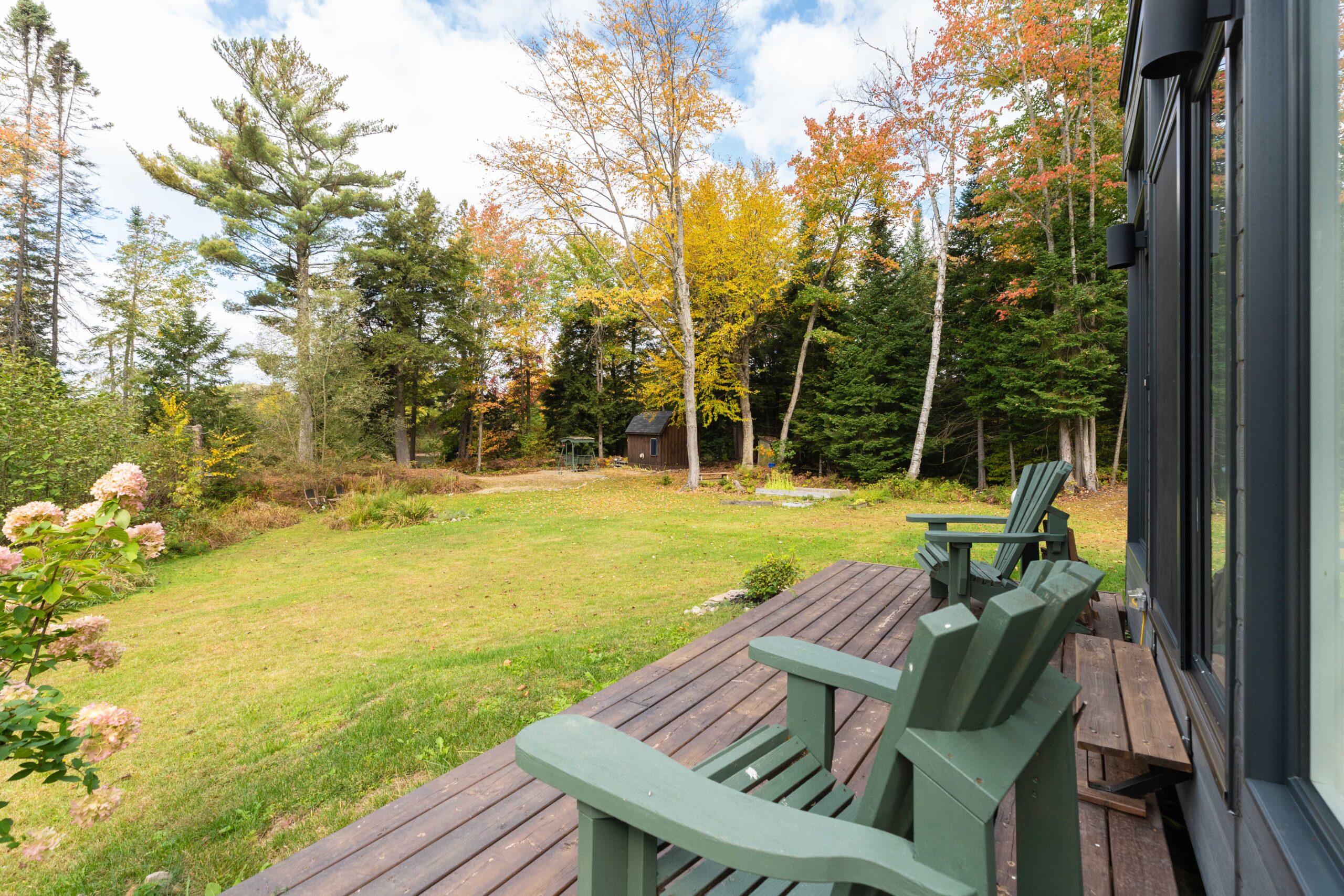 Green Muskoka chairs on a slim deck look out onto a grassy lawn