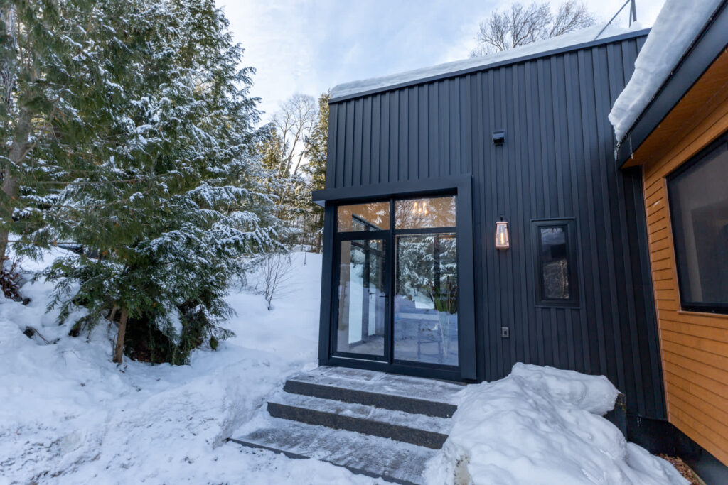 A black wood panelled cottage with a large glass door