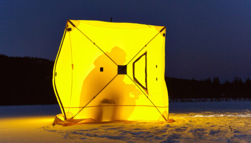 A yellow ice fishing hut with a person inside, in darkness