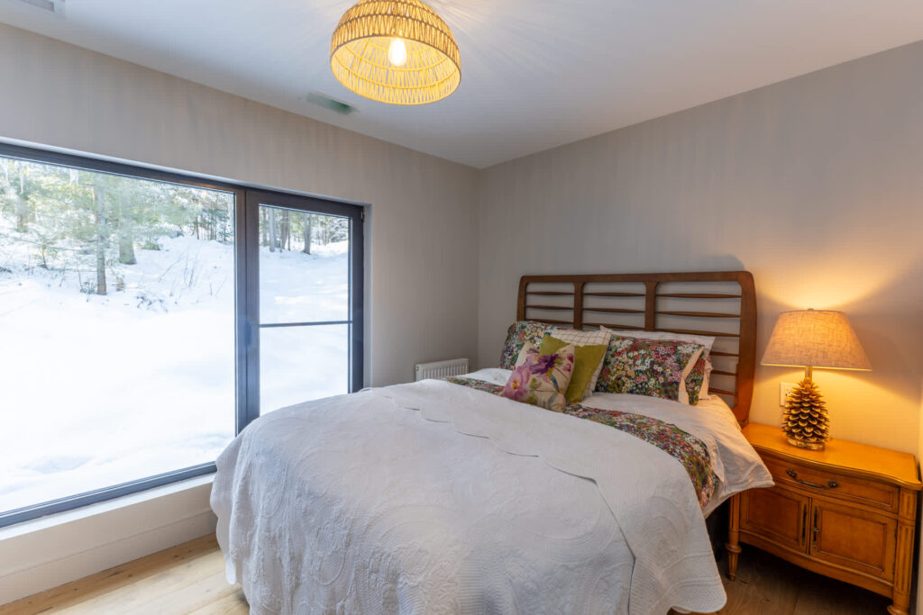 A white bed with colourful pillows next to a large window