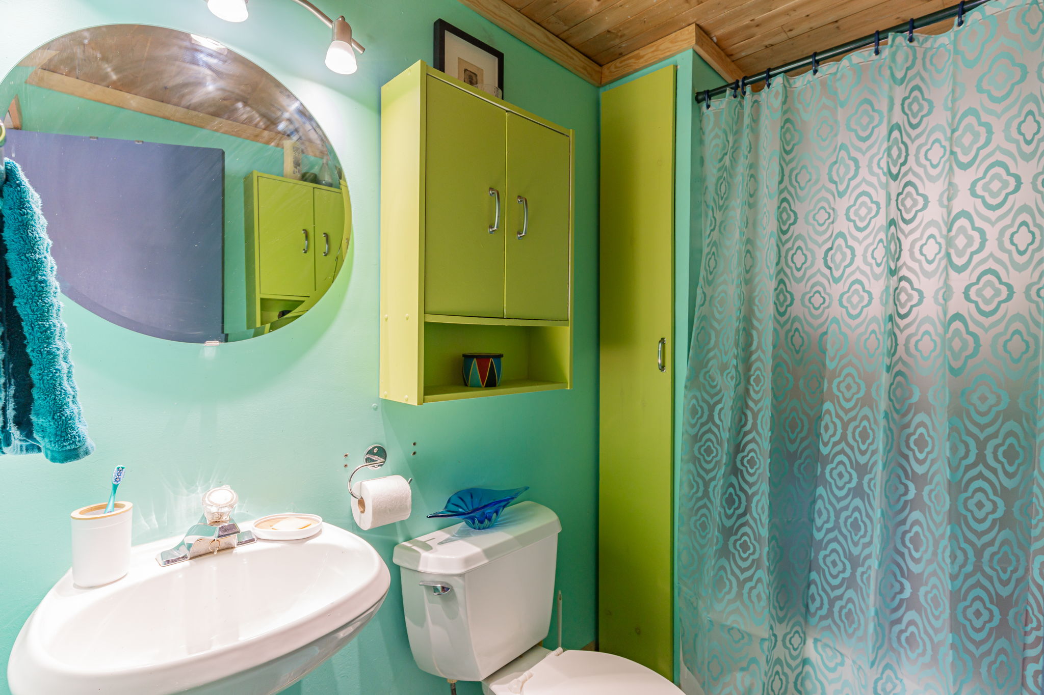 A teal bathroom with green cabinets and a green shower curtain