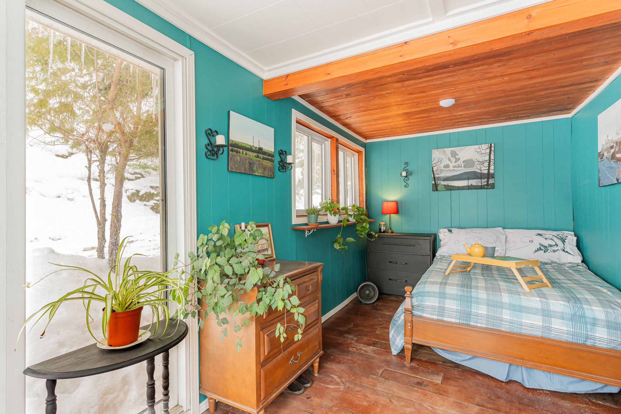 A teal bedroom with a blue plaid bed. The bed faces windows