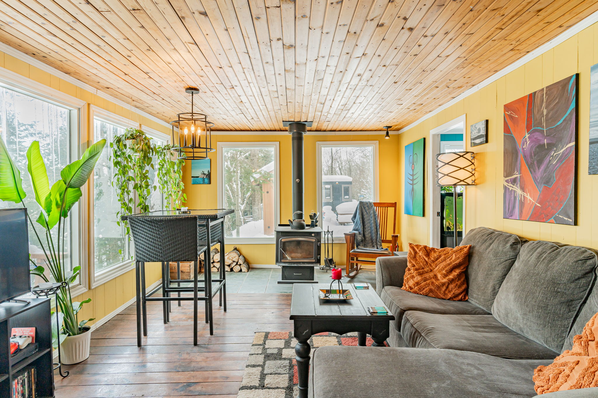 A spacious yellow living space with a grey couch and high-top dining set