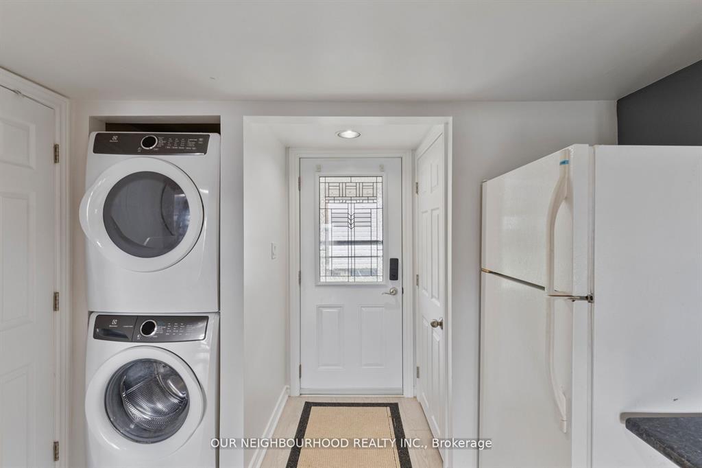 A white front door with stacked laundry machines on the left and a white fridge on the right
