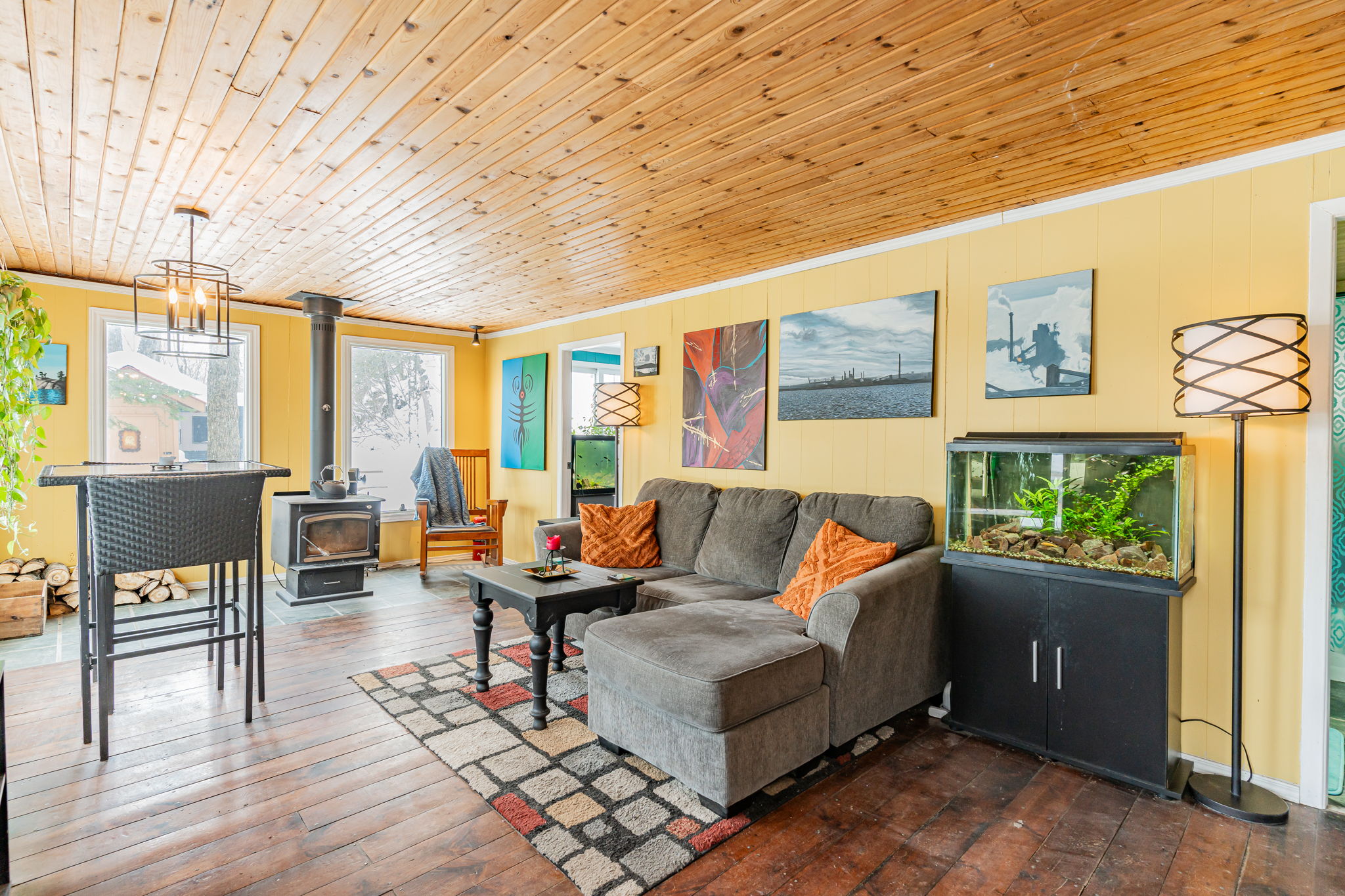 A spacious yellow living space with a grey couch and high-top dining set