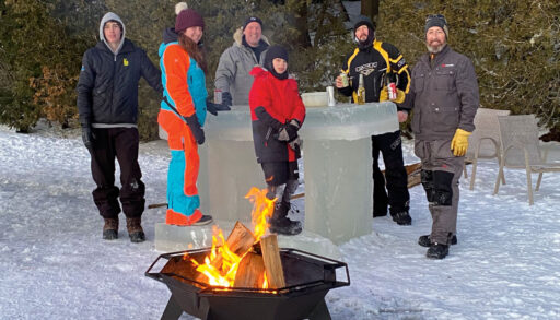 a group of people in snowsuits tand around a bar made of ice