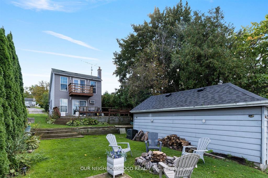A two-story cottage sits on a grassy property with a fire pit and Muskoka chairs