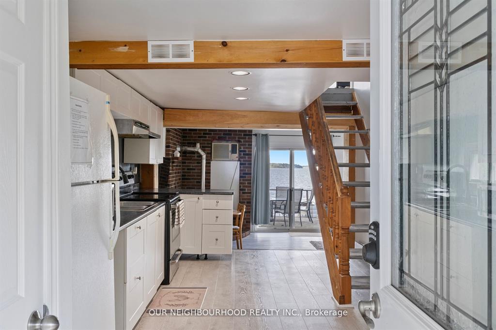 A white kitchen with black countertops and tiled floors. Wooden steps lead upstairs