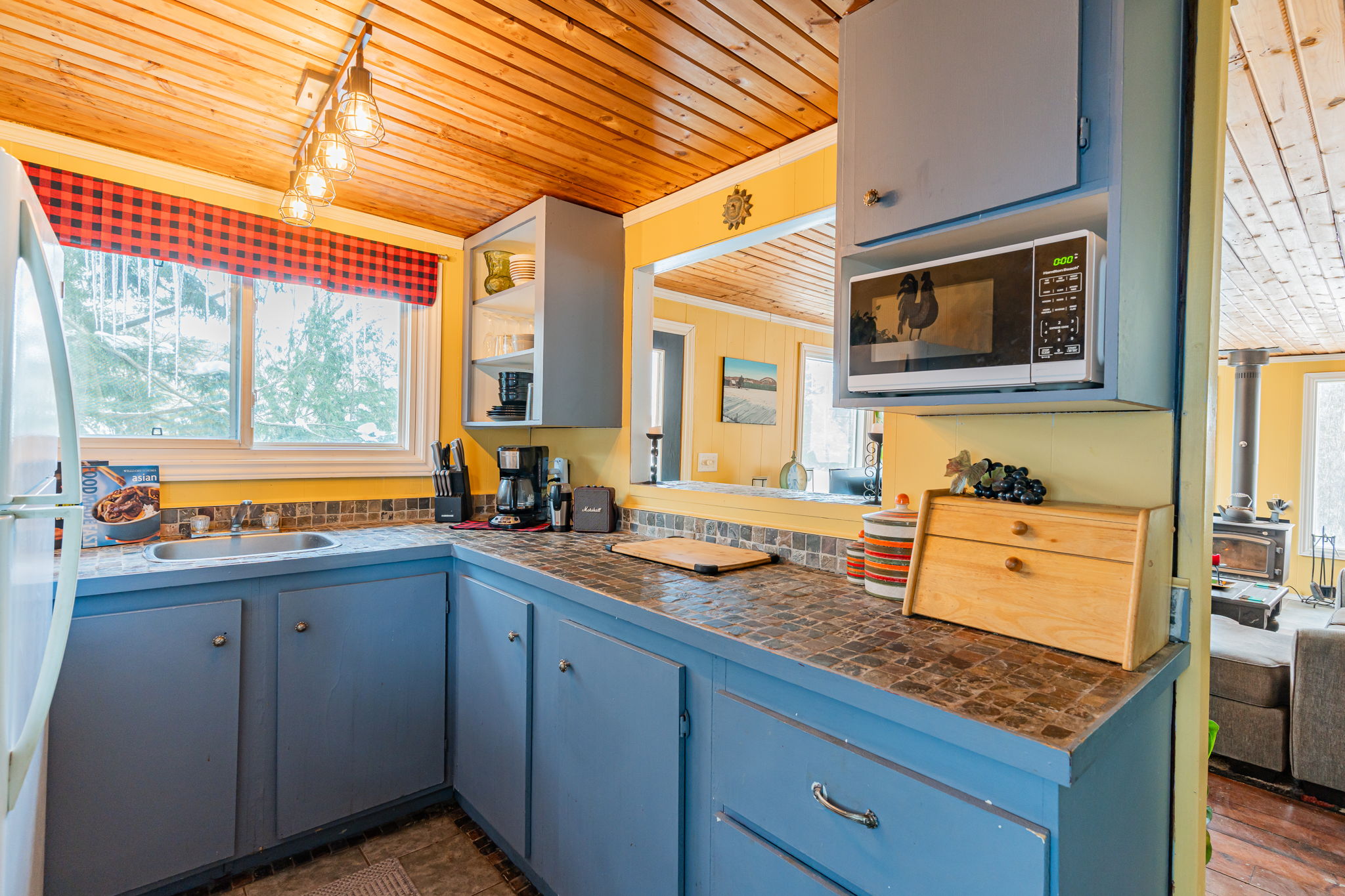 A small kitchen with blue cabinets. A pass-through window is open to the living room