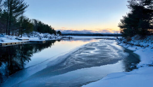 A snowy, partially frozen lake in winter with the sun setting