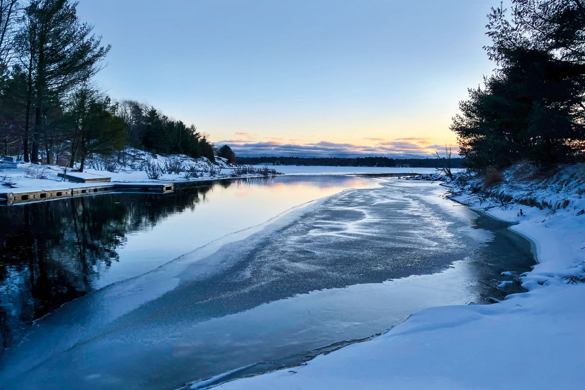 A snowy, partially frozen lake in winter with the sun setting