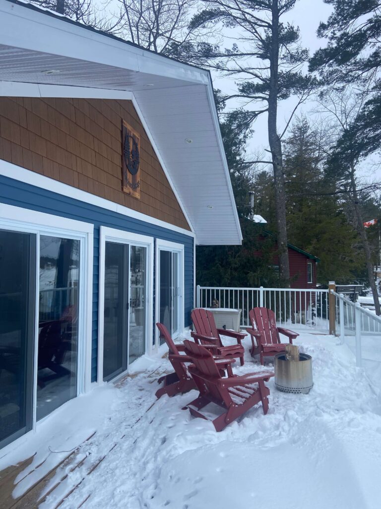 Red Muskoka chairs sit on a snowy back deck