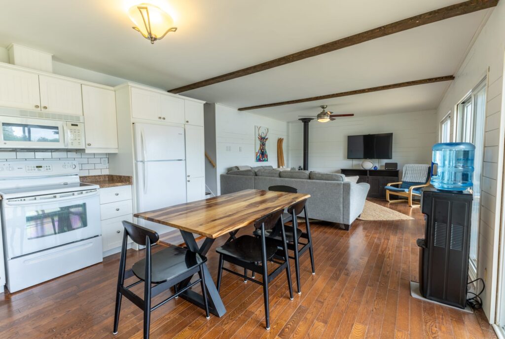 A long wood table in an open-concept white kitchen faces a grey couch