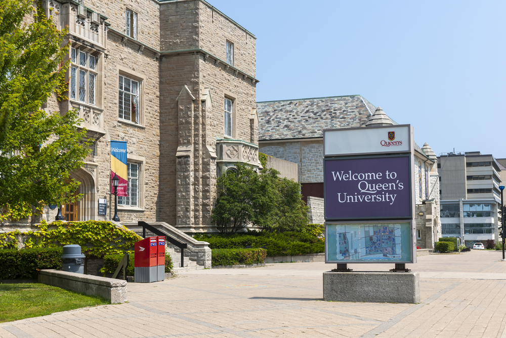 The logo of Queen's University in front of a main campus building in Kingston, Ont.