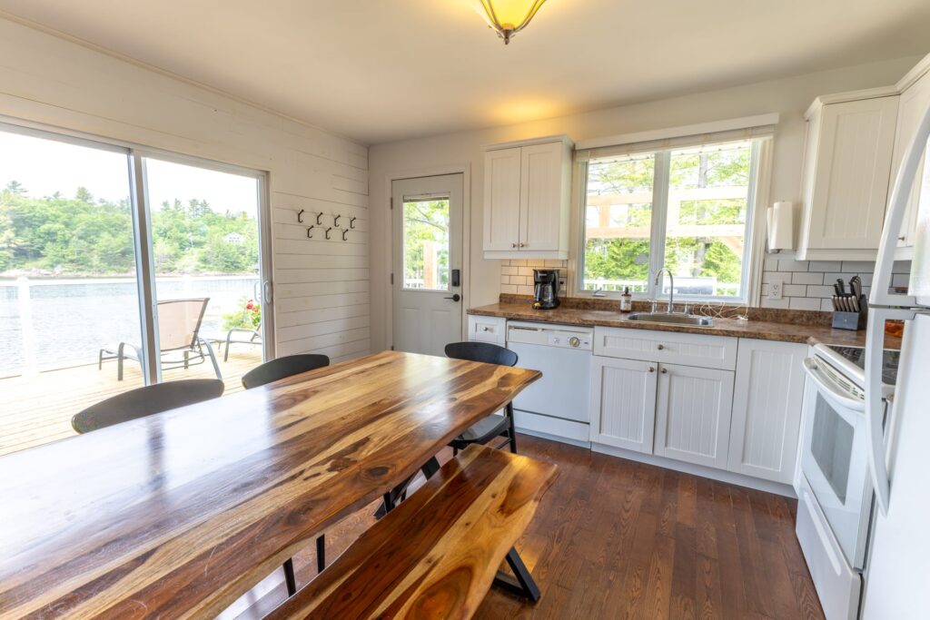 A long wood table in an open-concept white kitchen faces a grey couch