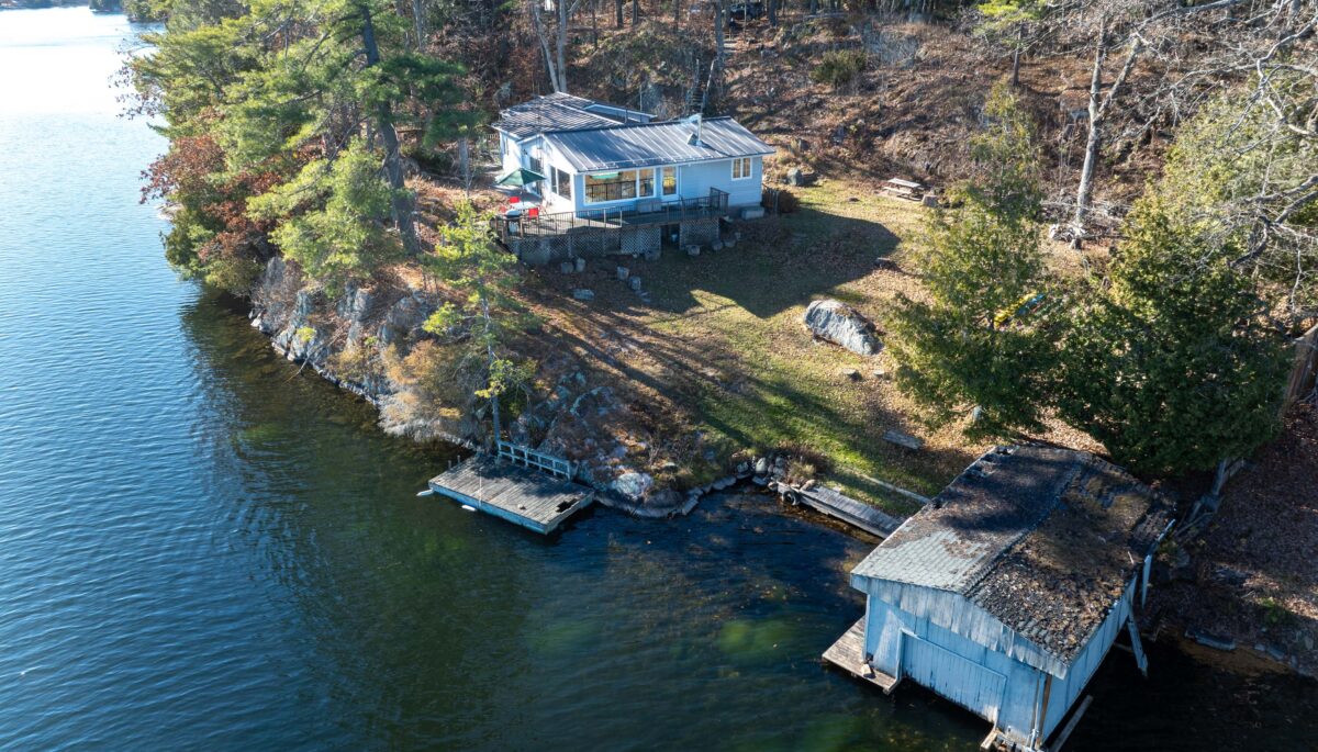 A cottage overlooking a lake. By the shoreline, a small dock and a boathouse