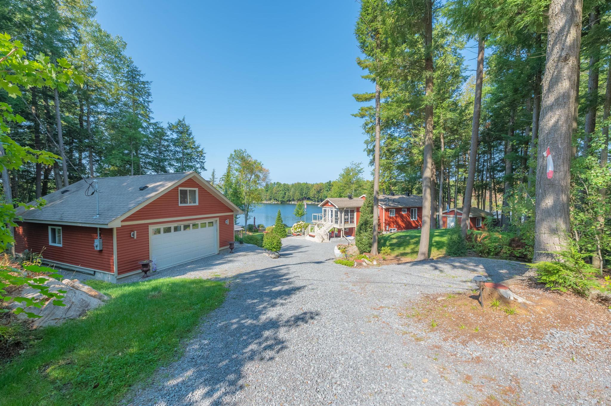 A scenic gravel driveway surrounded by tall trees, leading towards the cottage with a view of the lake in the distance.
