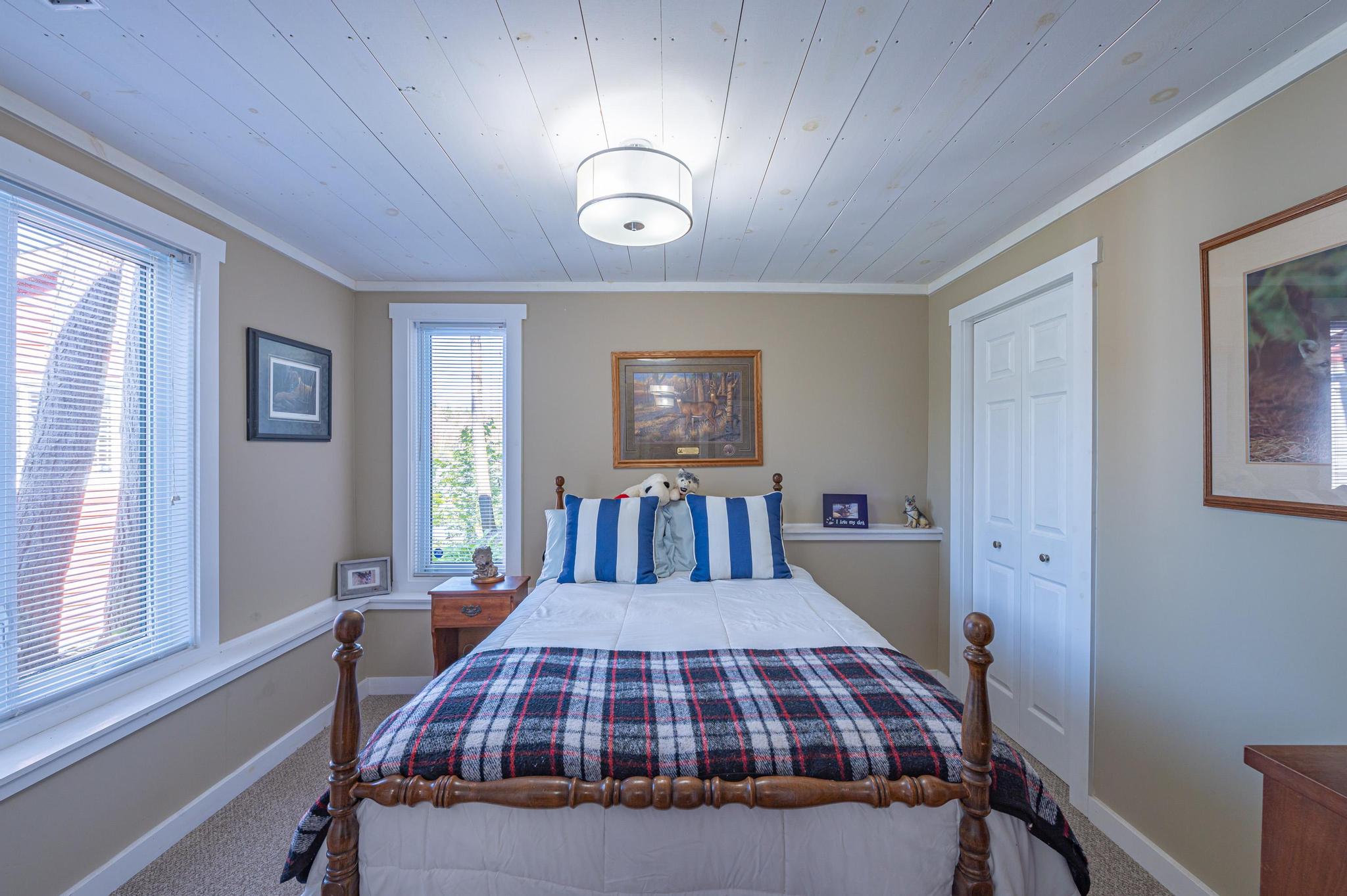 A bright and airy guest bedroom with a neatly made bed and large windows.