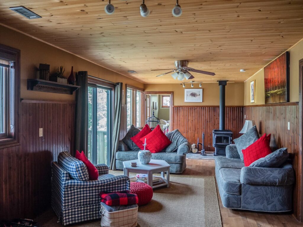 Grey couches with red pillows face each other in a wood-paneled room