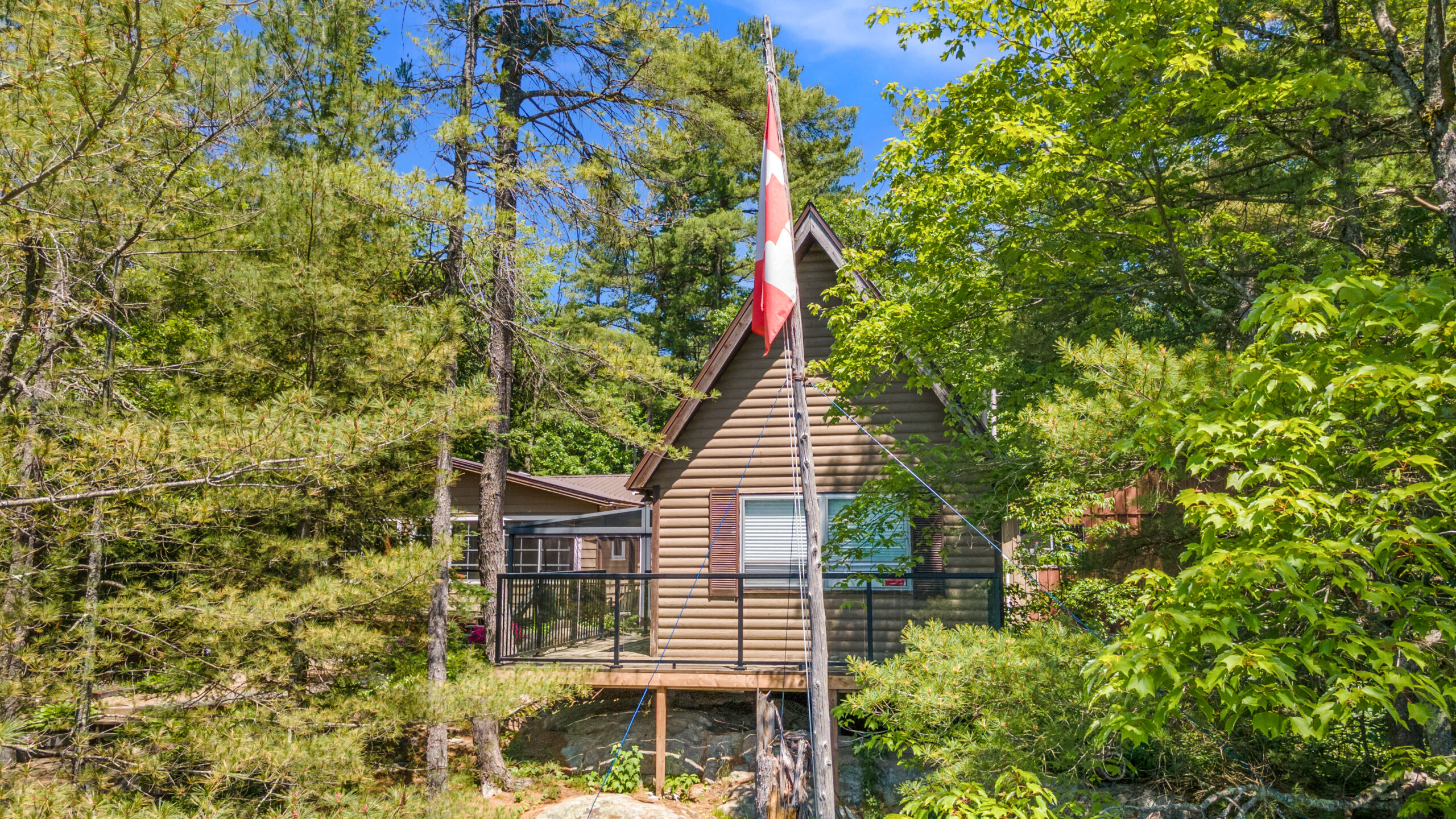 A wood-paneled cabin in a forest. A Canada flag waves in front.