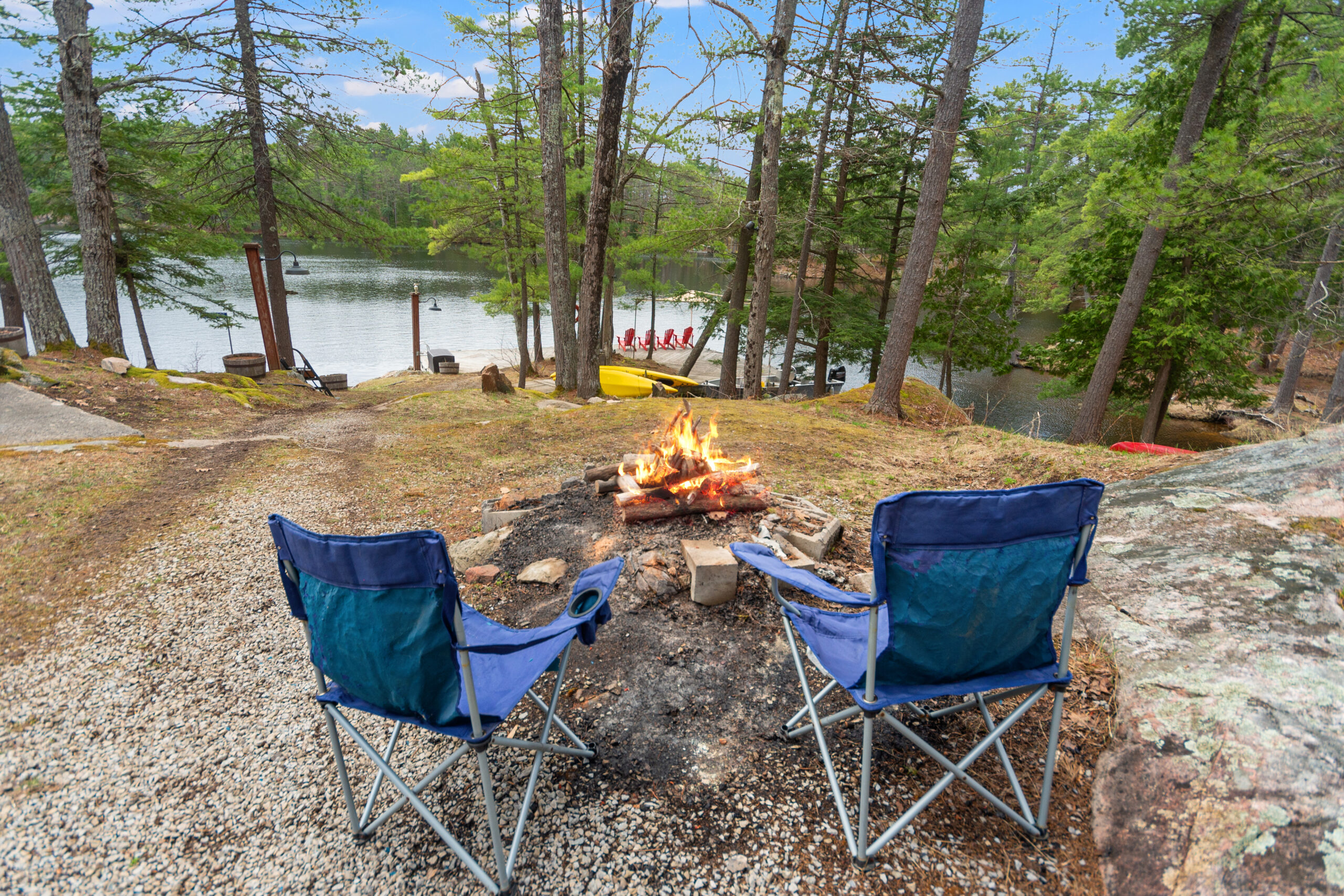 Two blue chairs face a roaring fire pit in the forest