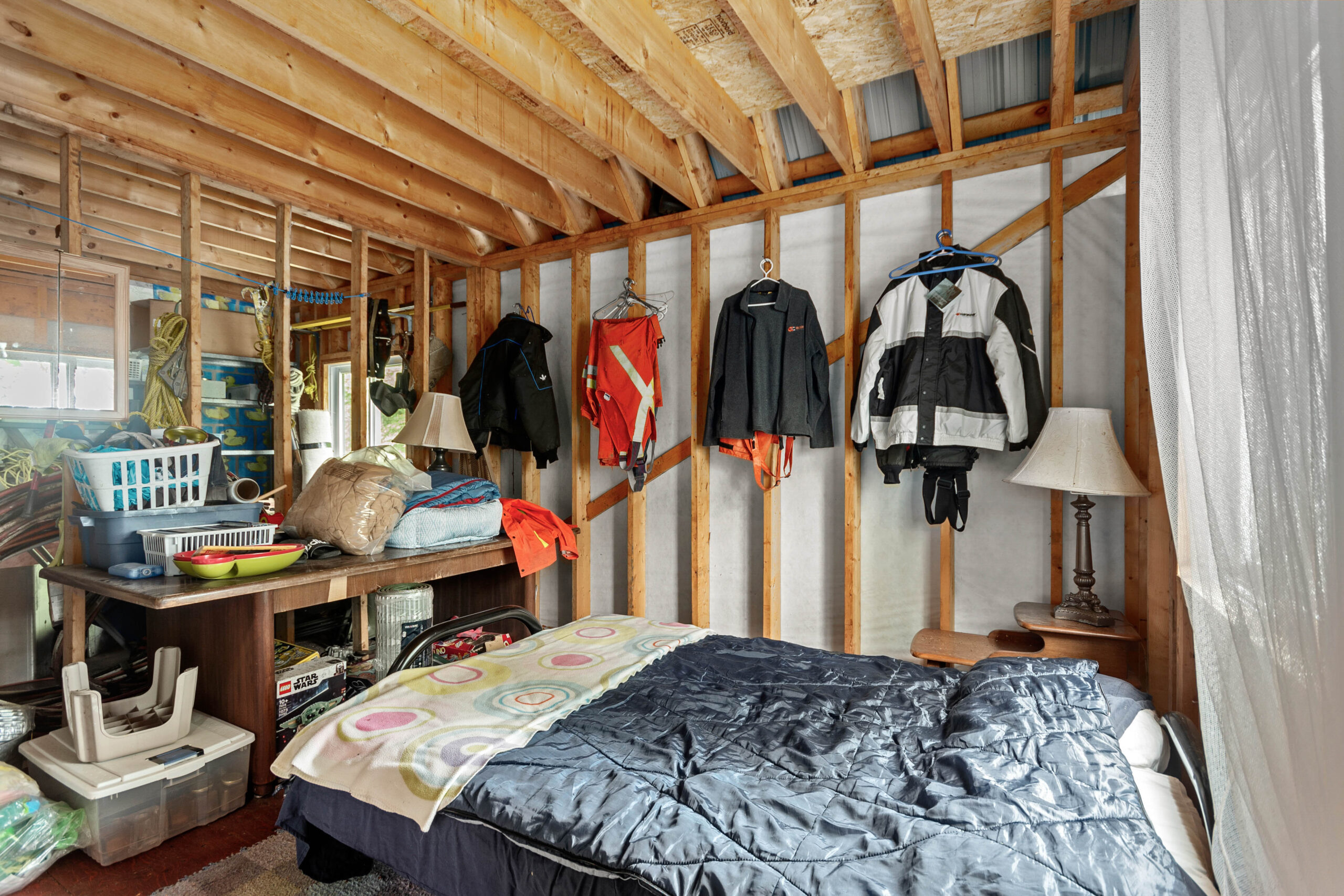 A bed sits along the side of a wood room with jackets hanging on the wall