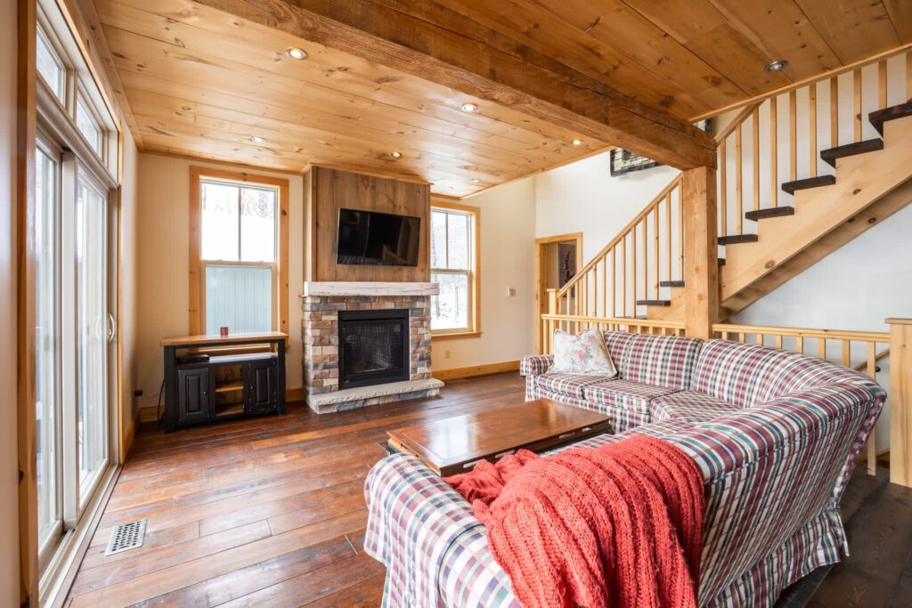 A plaid couch faces a stone fireplace with a TV hanging above in a wood room