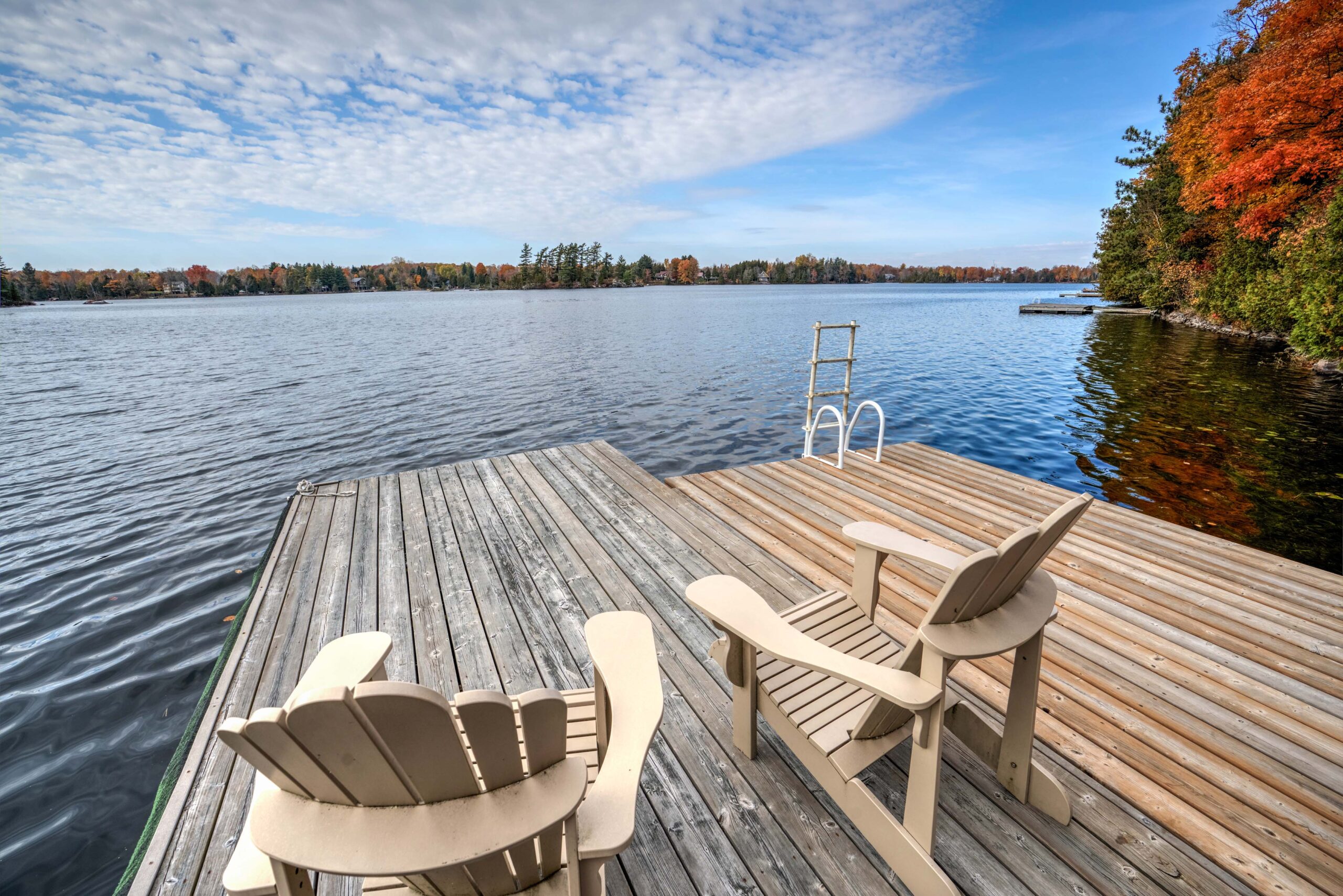 A dock with two white Muskoka chairs on the lake