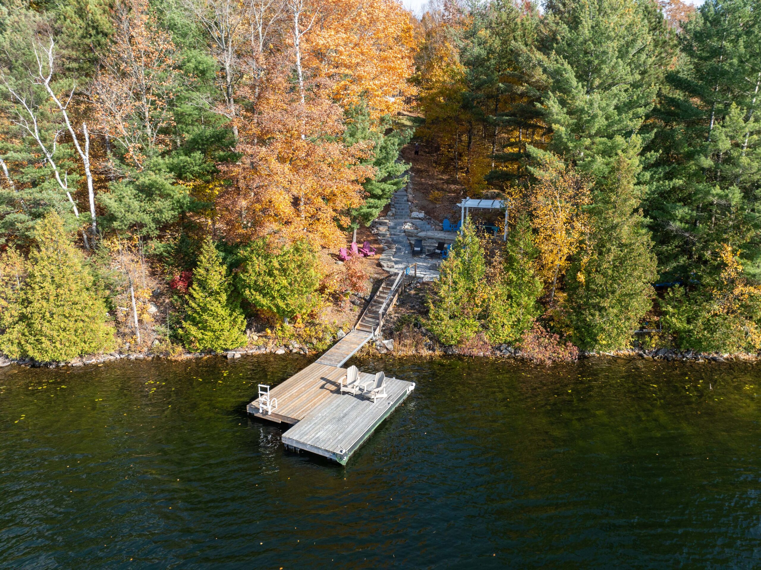 Aerial view of a dock jutting out from an autumn forested shoreline