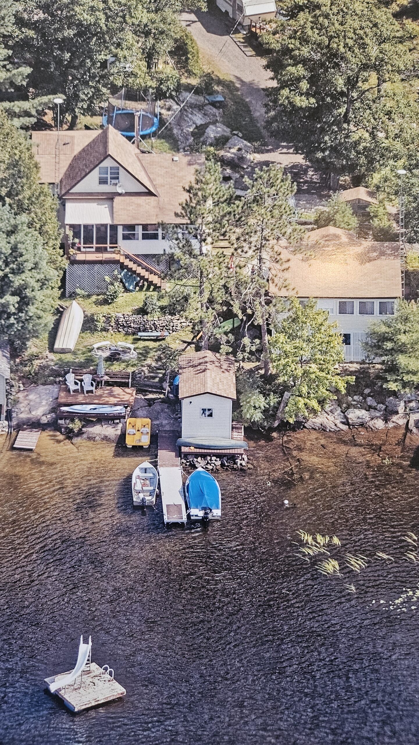 A vibrant summer scene of the property, featuring a dock, boathouse, and clear lake water, perfect for swimming, boating, and lakeside relaxation.