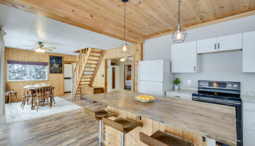 A beautifully updated open-concept kitchen with wood-paneled ceilings, modern white cabinetry, pendant lighting, and a large island with bar seating.