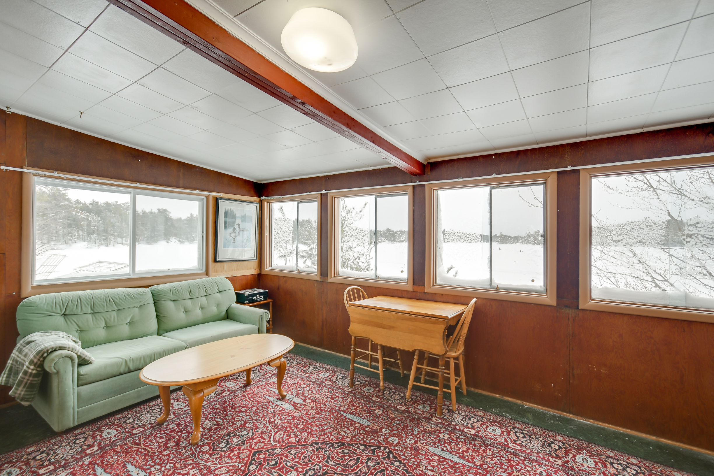 A rustic sitting area with large windows providing sweeping views of the frozen lake, featuring cozy furnishings perfect for relaxing.