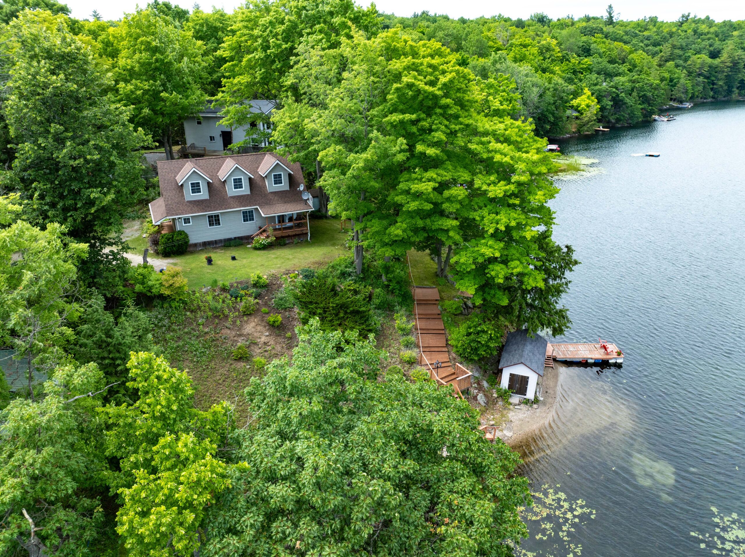 A paneled-cottage with three upper windows is set back from the lake on a lush green property