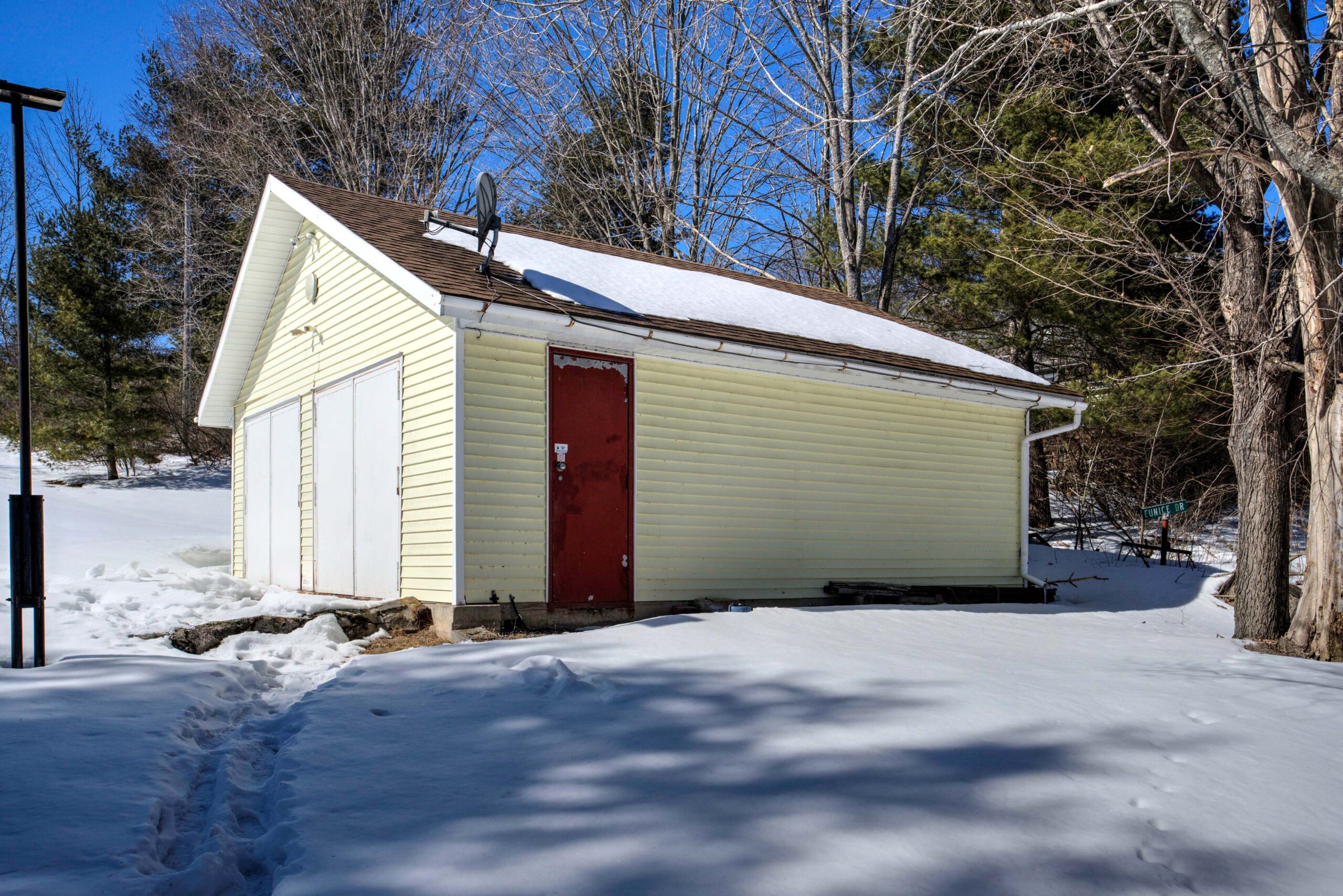A pale yellow double-garage with a red side door in a snowy yard