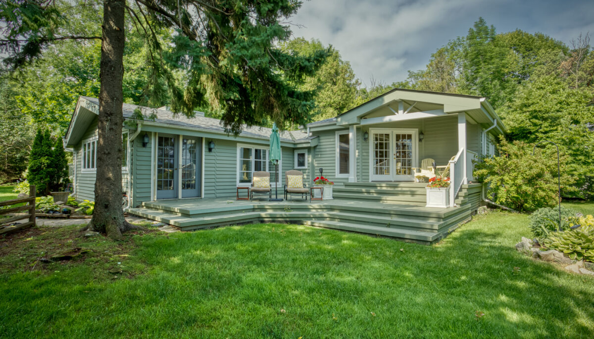 A green-paneled cottage with white trim and steps to a grassy lawn