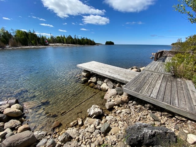 A dock juts out in a blue lake with a rocky shoreline