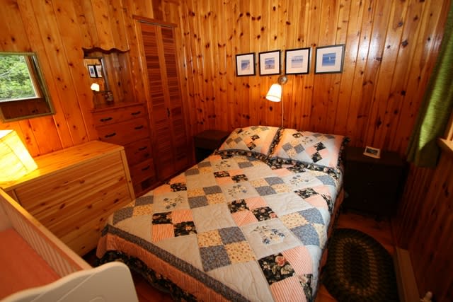 A bed in a wood-paneled room is covered in a patterned quilt