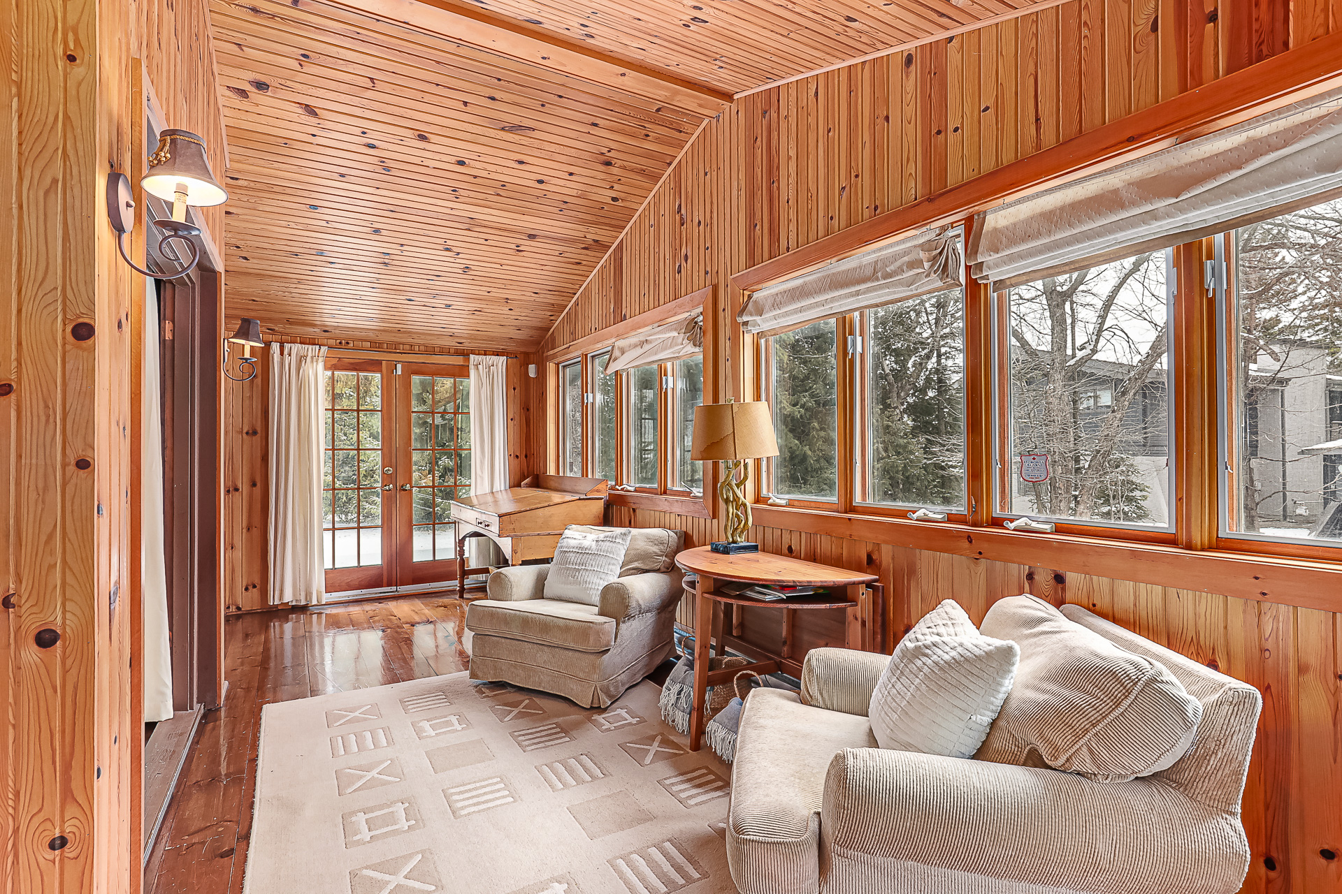 Two white chairs with a wood side table in between face away from a wood-paneled wall of windows