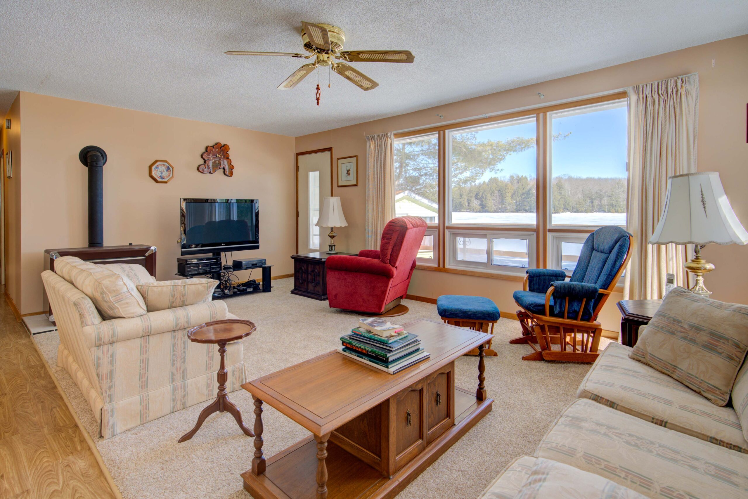 A cream couch, red chair, and blue rocking chair face a TV in a bright living room