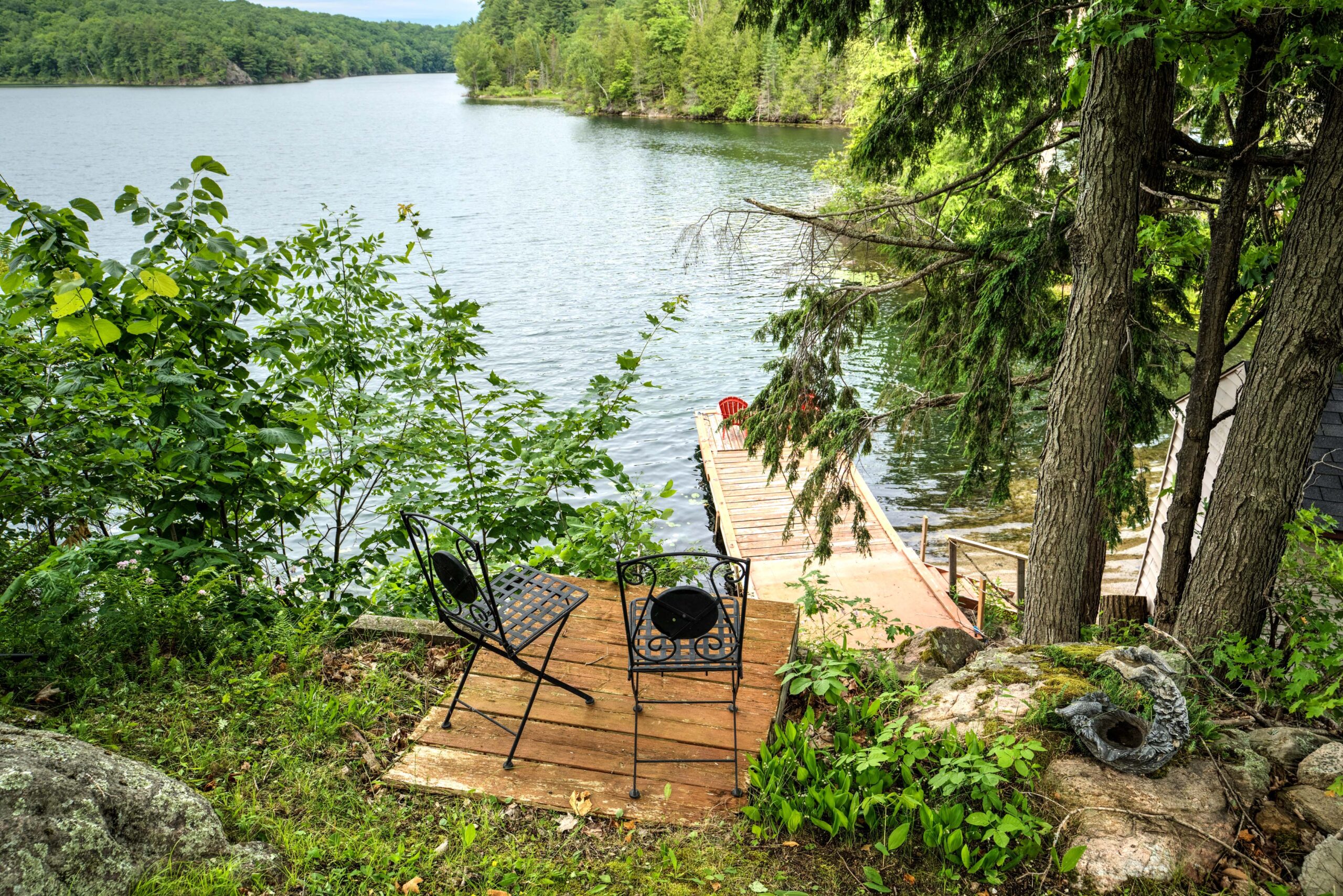 A small wood platform with two black metal chairs face the lake