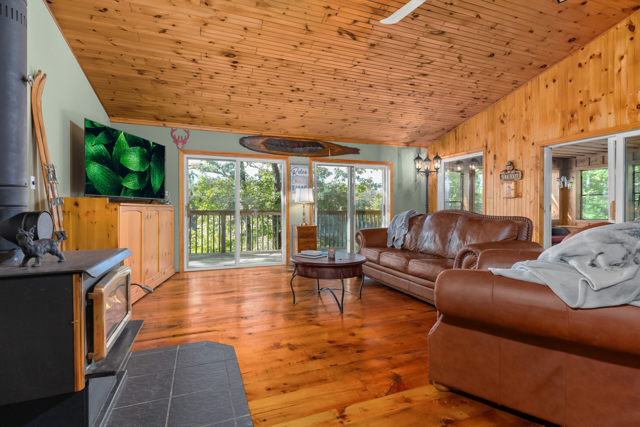 Rustic-style living room with leather sofas, wood-burning stove, and large windows.