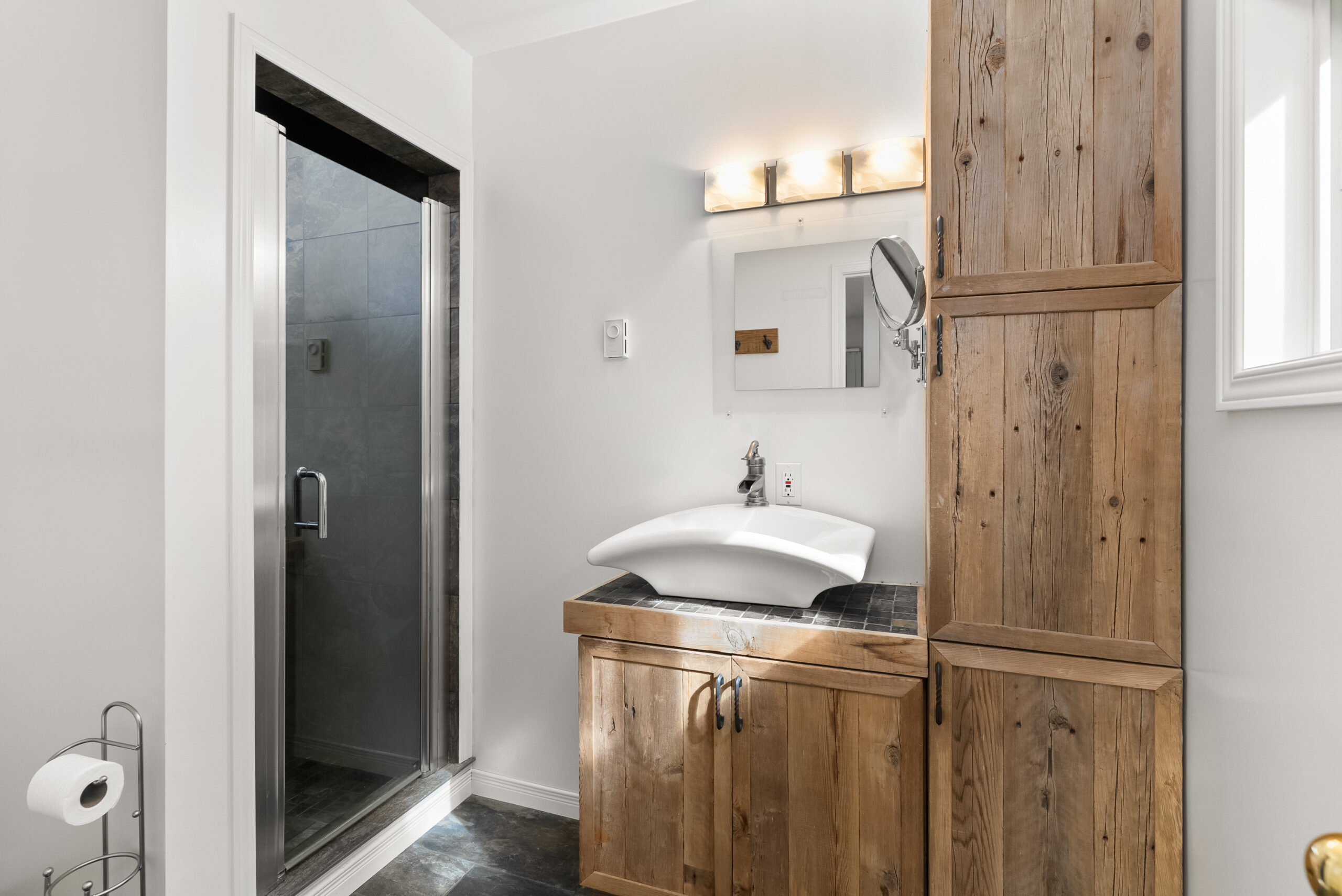 Bathroom with walk-in shower, vessel sink, and wooden cabinetry.