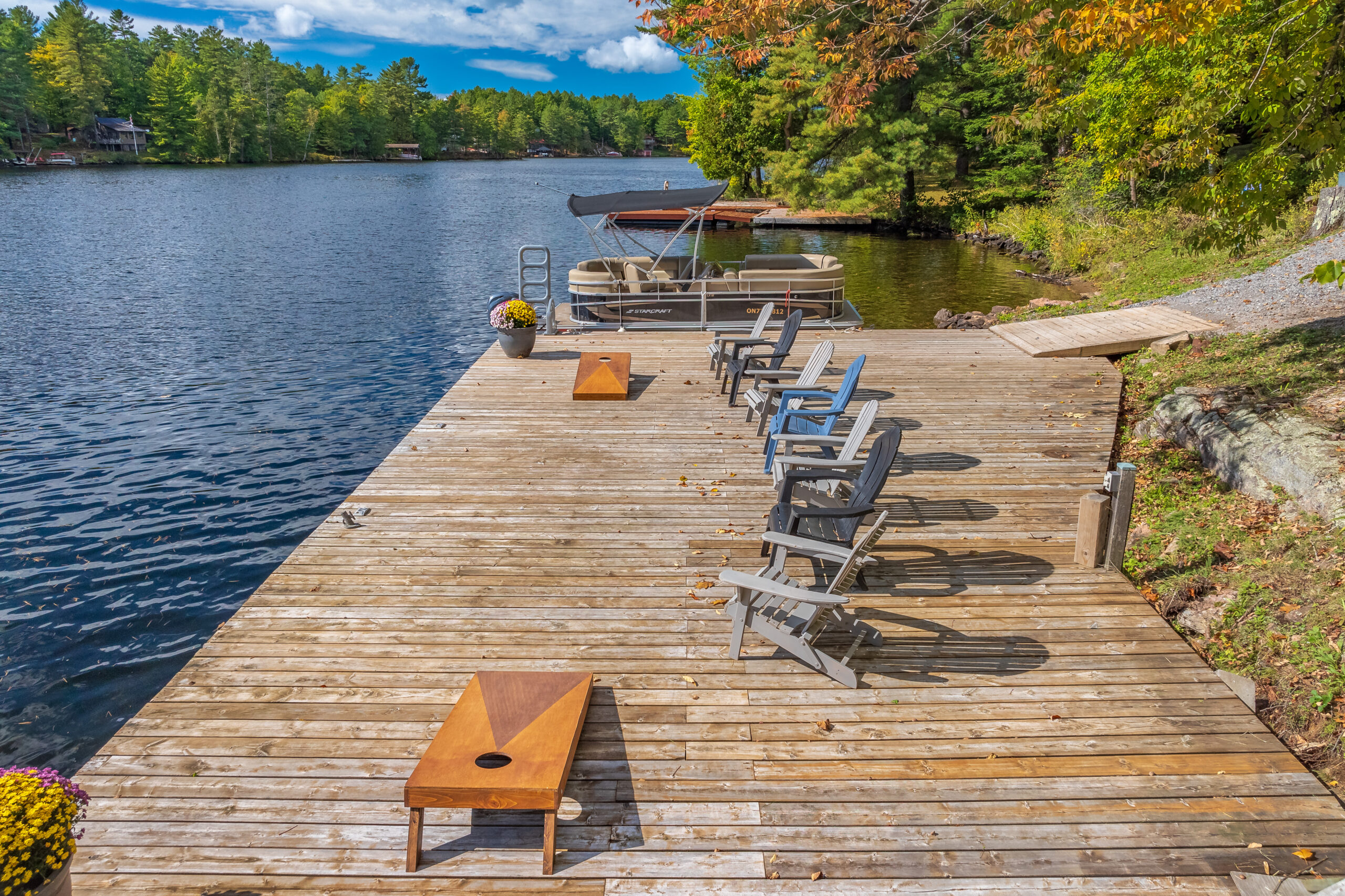 Wide wooden dock with lounge chairs set up by calm waters and forested shoreline.