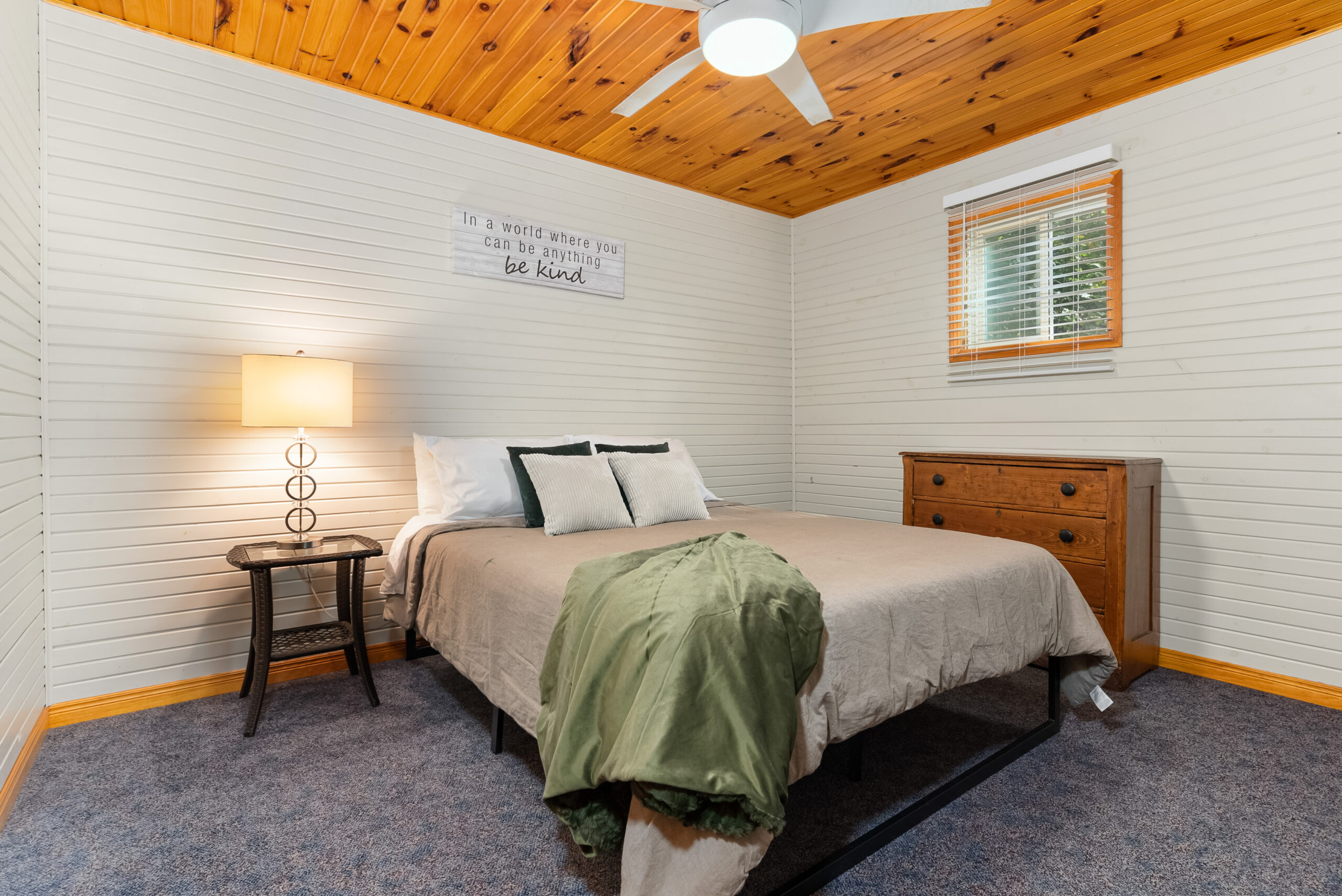 Bedroom with white shiplap walls, wood ceiling, and queen bed.