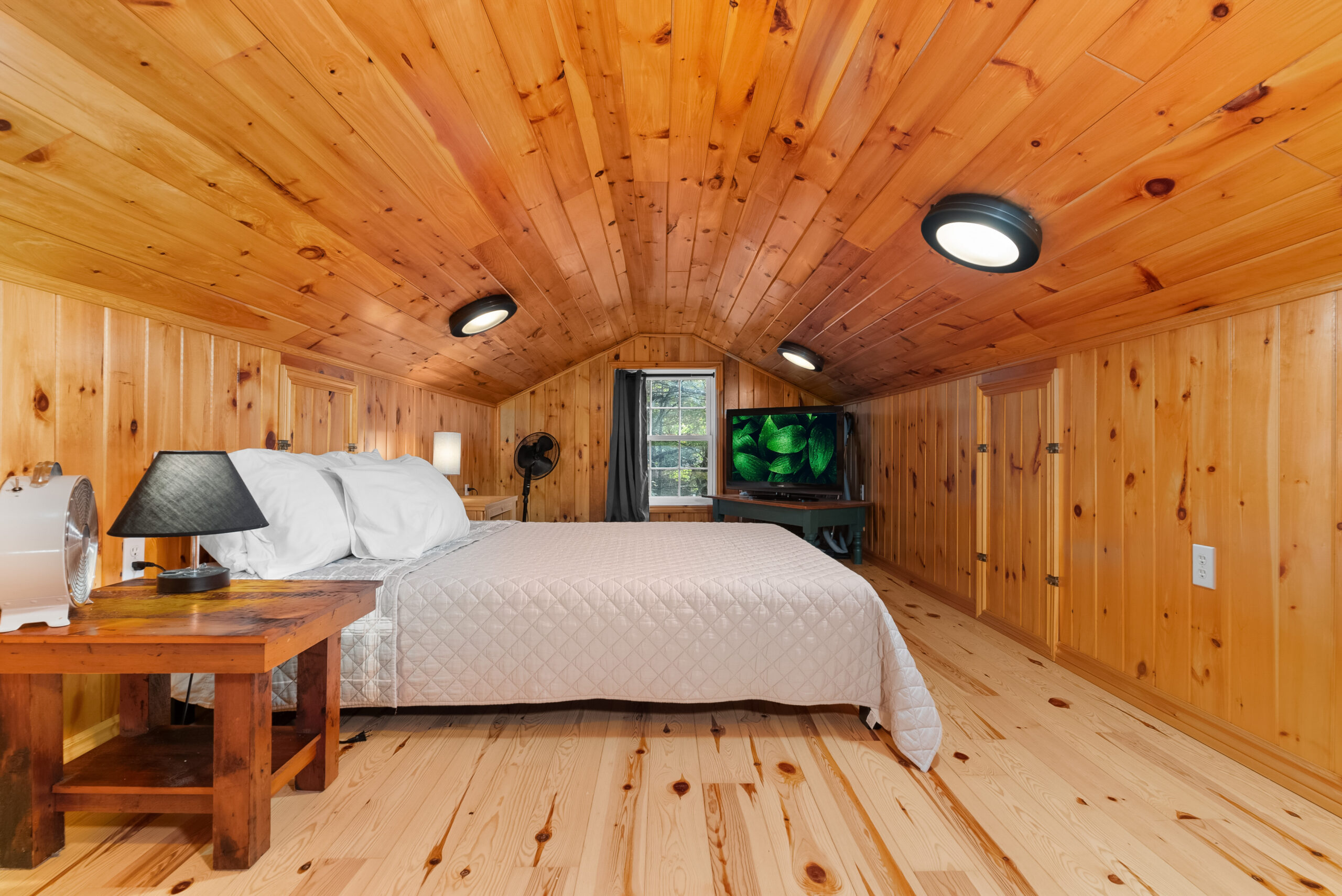 Cozy loft bedroom with sloped pine ceiling and a single bed.