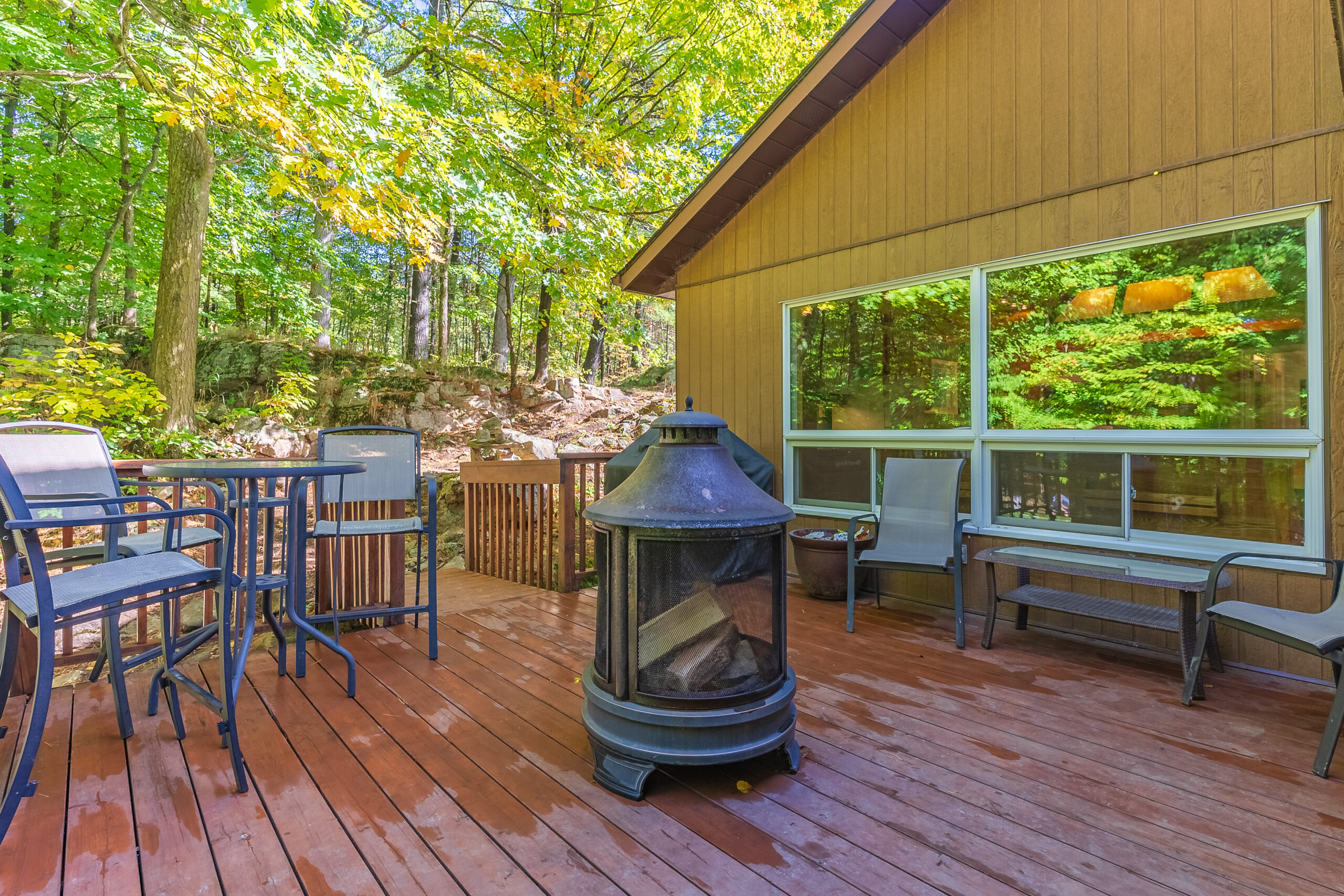 Outdoor deck with patio furniture, fire pit, and forest backdrop.