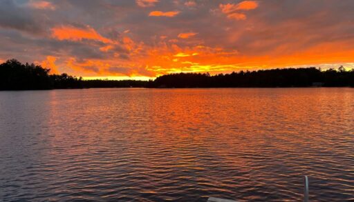 Fiery orange and gold sunset reflecting over Kahshe Lake, viewed from a dock with a boat motor in the foreground